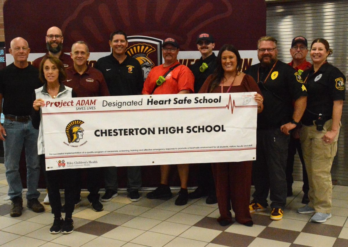 Pictured are the staff at Chesterton High School along with faculty from Project ADAM celebrating the certification. Holding the banner are CHS Nurse, Marie Kirchner (Left) and CHS Nurse, Brittany Smith (Right). Image provided through CHS Staff.