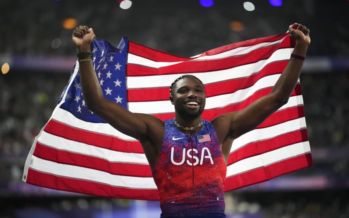 Noah Lyles holds the US flag following his 100m first place finish at the 2024 Olympics.